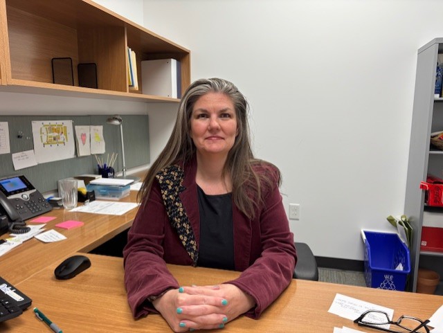 This image matters because it shows my workspace and the calm confidence I feel in my maroon jacket at my organized desk.