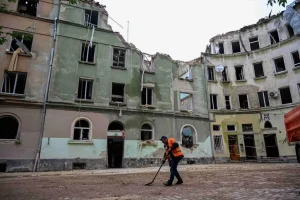 This image matters to me as it shows resilience—someone in an orange vest cleaning amid ruined, partially destroyed buildings.